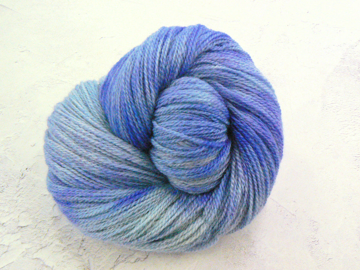 A skein of variegated yarn with a color-shifting gradient from light icy blue to medium and deep blue, photographed on a textured off-white background.