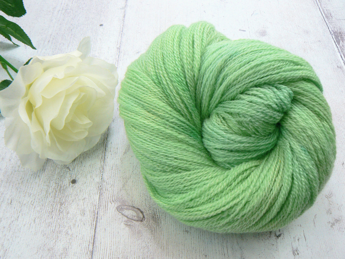 A ball of light mint green yarn displayed on a white wooden surface next to a white rose.
