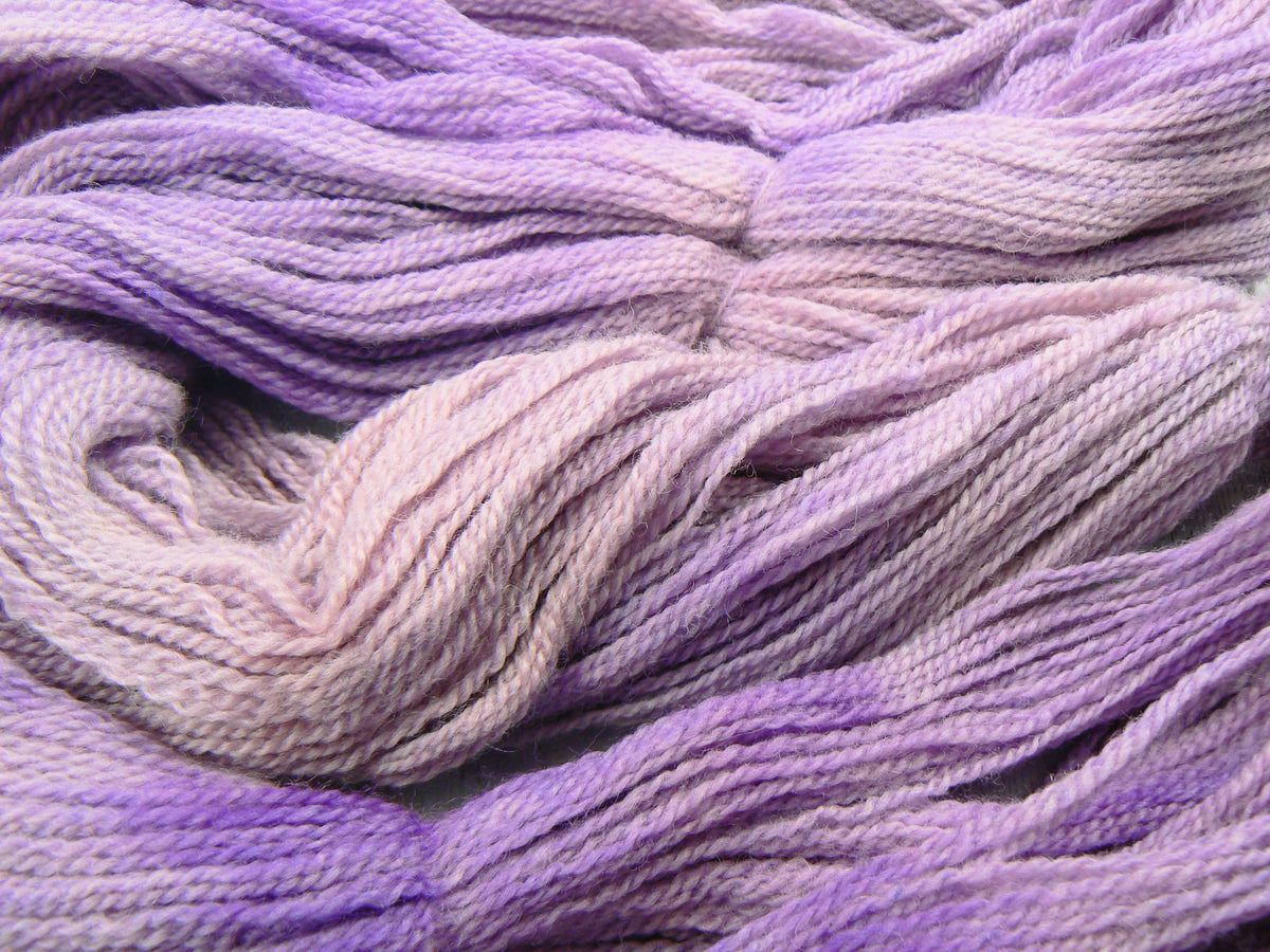 A close-up of twisted yarn in a soft lavender to pale pink gradient, filling the frame.