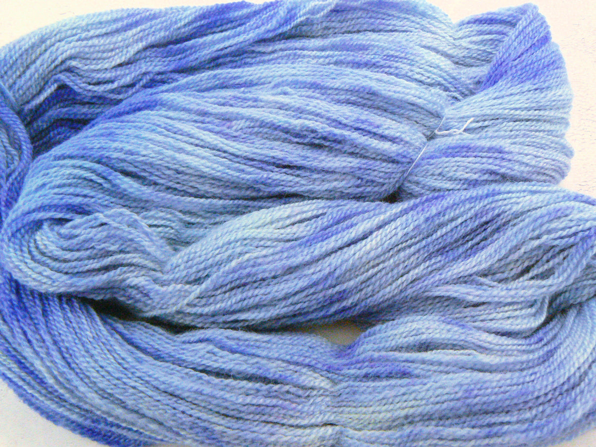 A close-up of variegated yarn in shades of light blue and purple, arranged in soft folds against a plain light background.