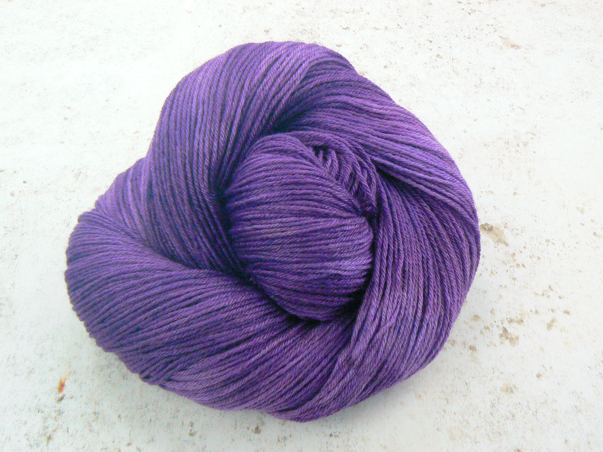 A single skein of purple yarn arranged in a spiral shape, photographed on a light off-white textured surface.