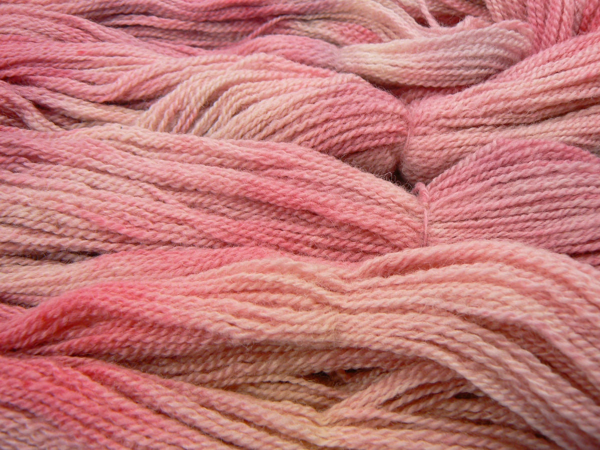 A close-up of soft, twisted yarn strands in a blended pink and peach gradient, filling the entire frame.