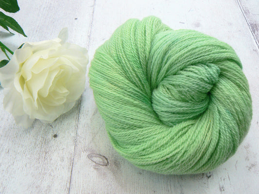 A ball of light mint green yarn displayed on a white wooden surface next to a white rose.