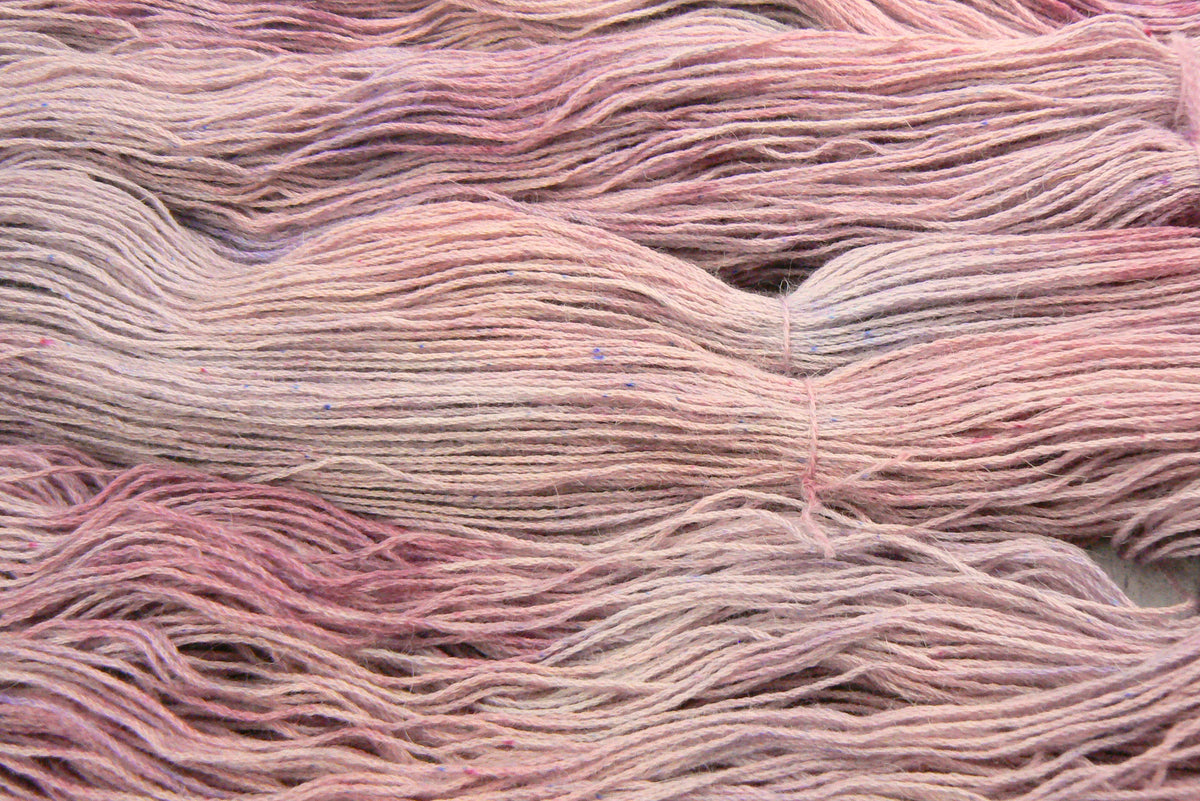 Close-up of bundled yarn strands in a soft dusty pink colourway, filling the frame.