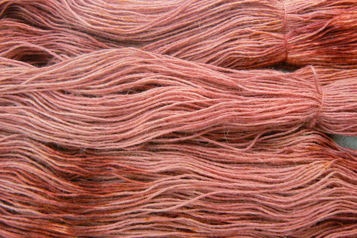 Close-up of variegated yarn in dusty rose, terracotta, and muted orange-brown tones.