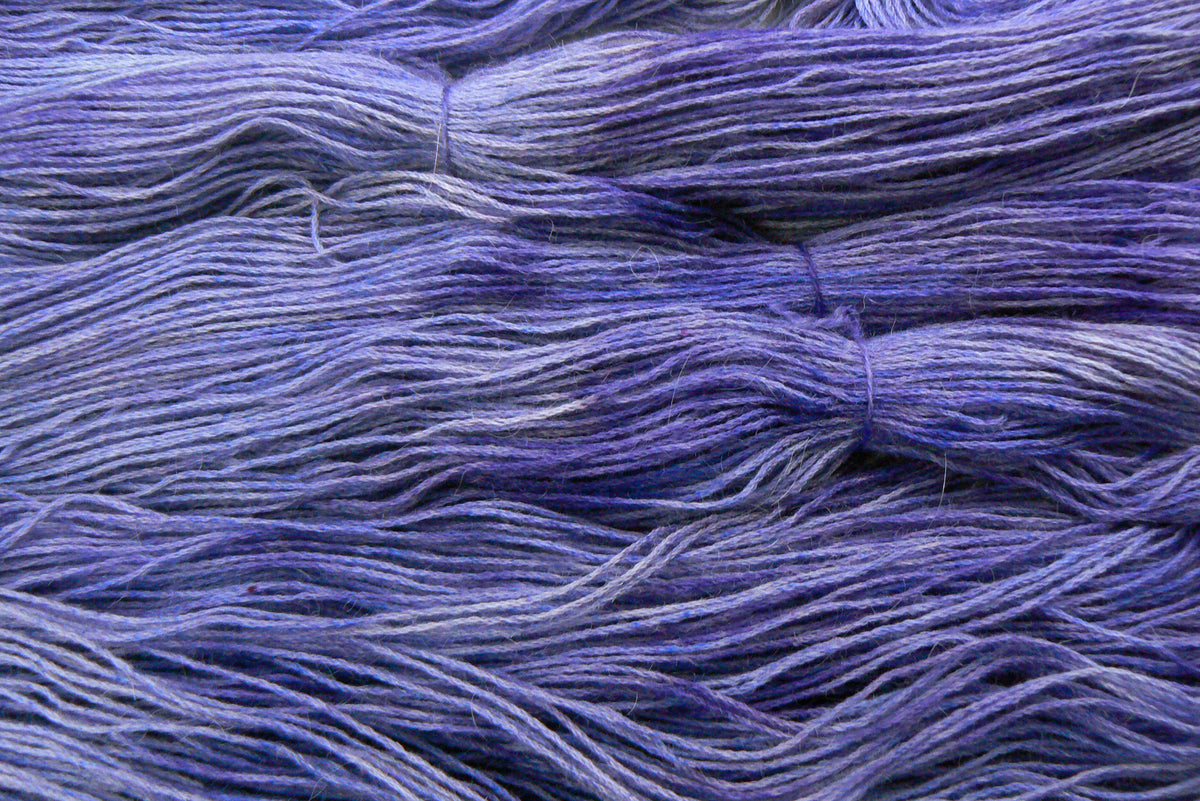 A close-up of bundled yarn strands in a heathered purple and blue colorway, showing the soft texture and variegated tones.