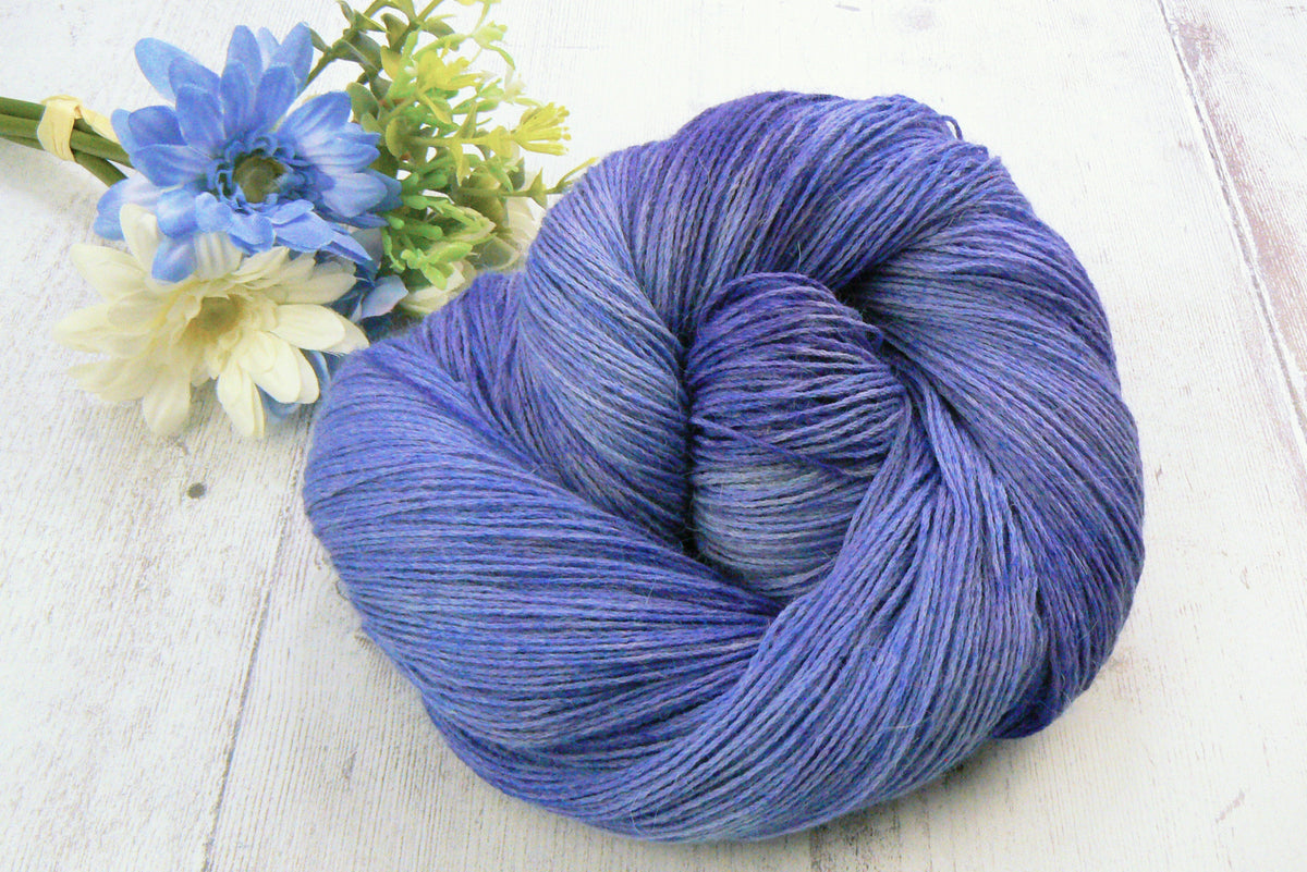 A skein of hand dyed yarn in shades of blue and lilac, alongside a bunch of blue and white flowers.