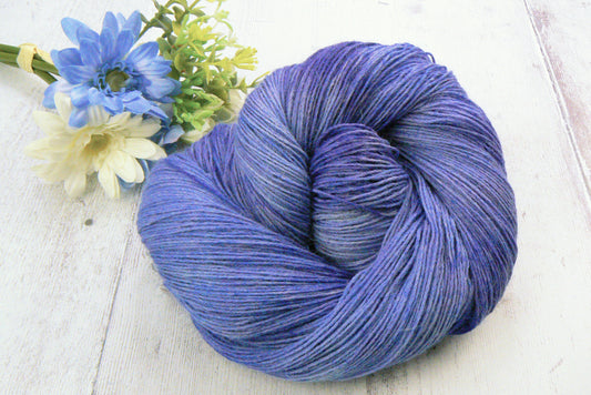 A skein of hand dyed yarn in shades of blue and lilac, alongside a bunch of blue and white flowers.