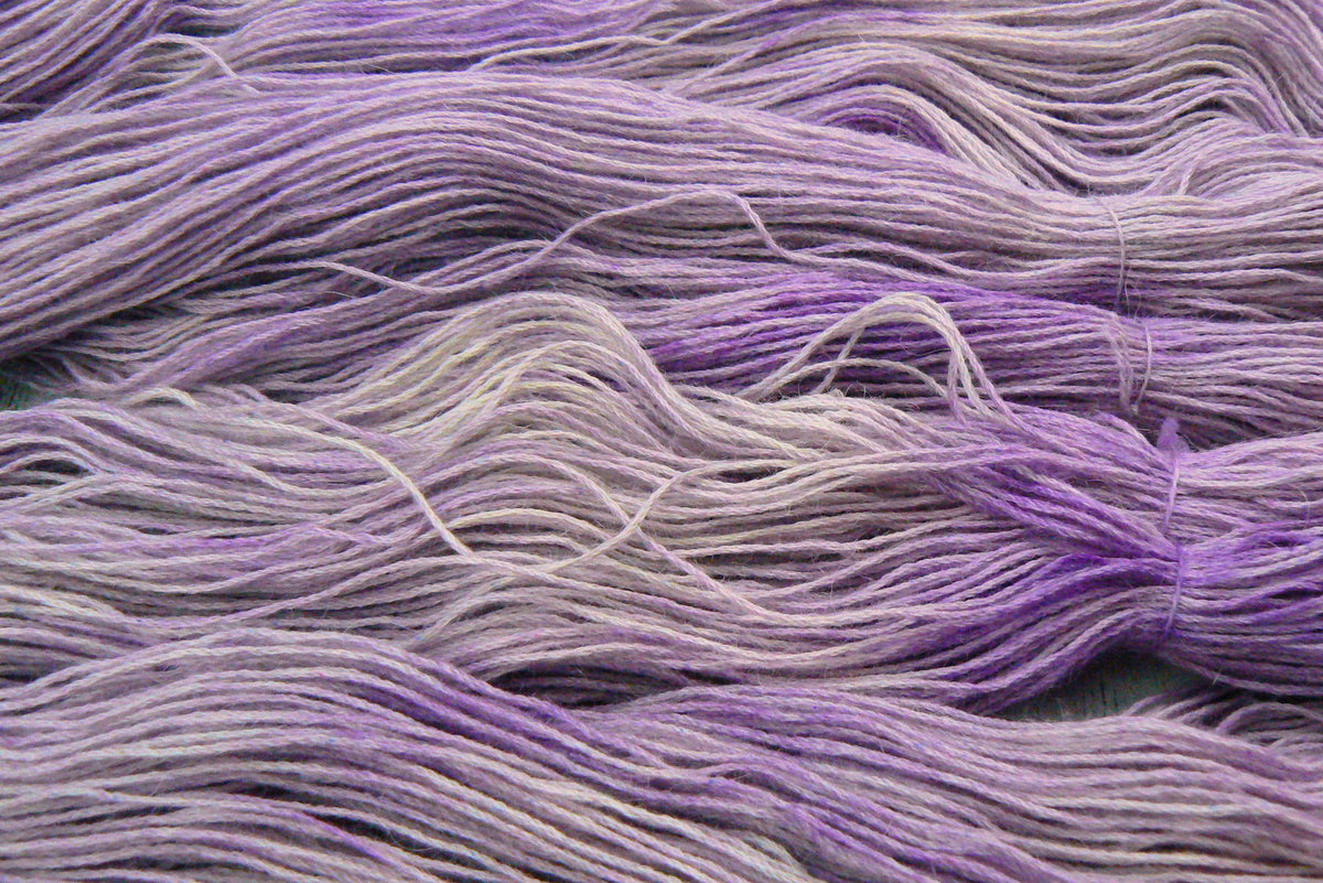 A close-up of multiple strands of soft yarn in a blended lavender and lilac colourway, bundled together.